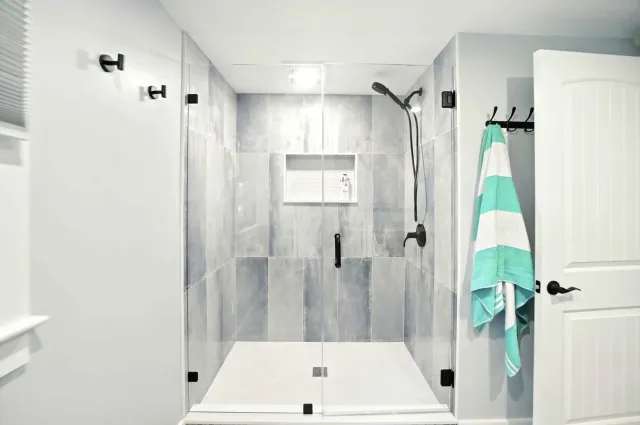 Modern bathroom with tiled shower, bench, towel hook, and open door