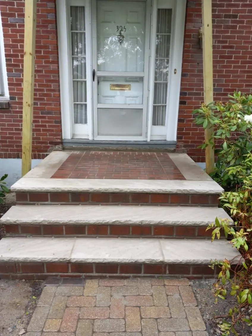 Brick steps leading to a front door with a screen. Wooden posts flank the door.