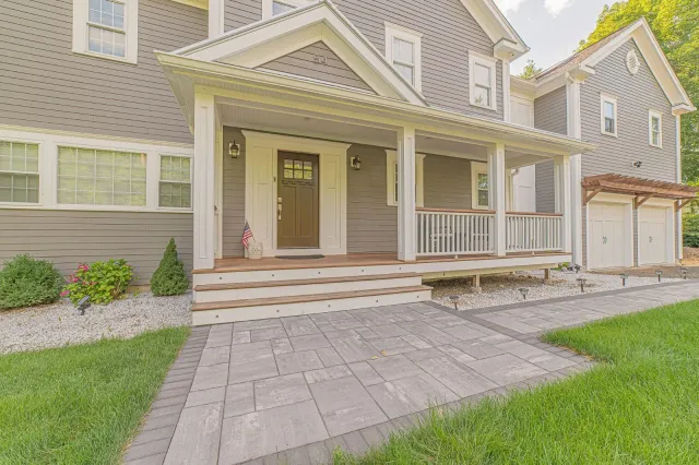 A large gray house with a large porch and a brick walkway leading to it.