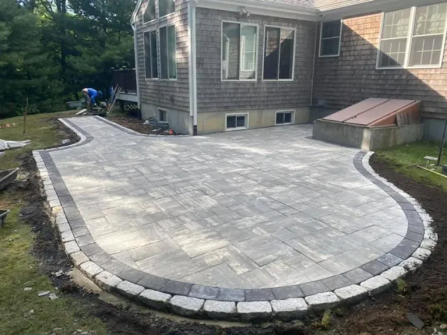 Rounded backyard paver patio finished beside a green lawn