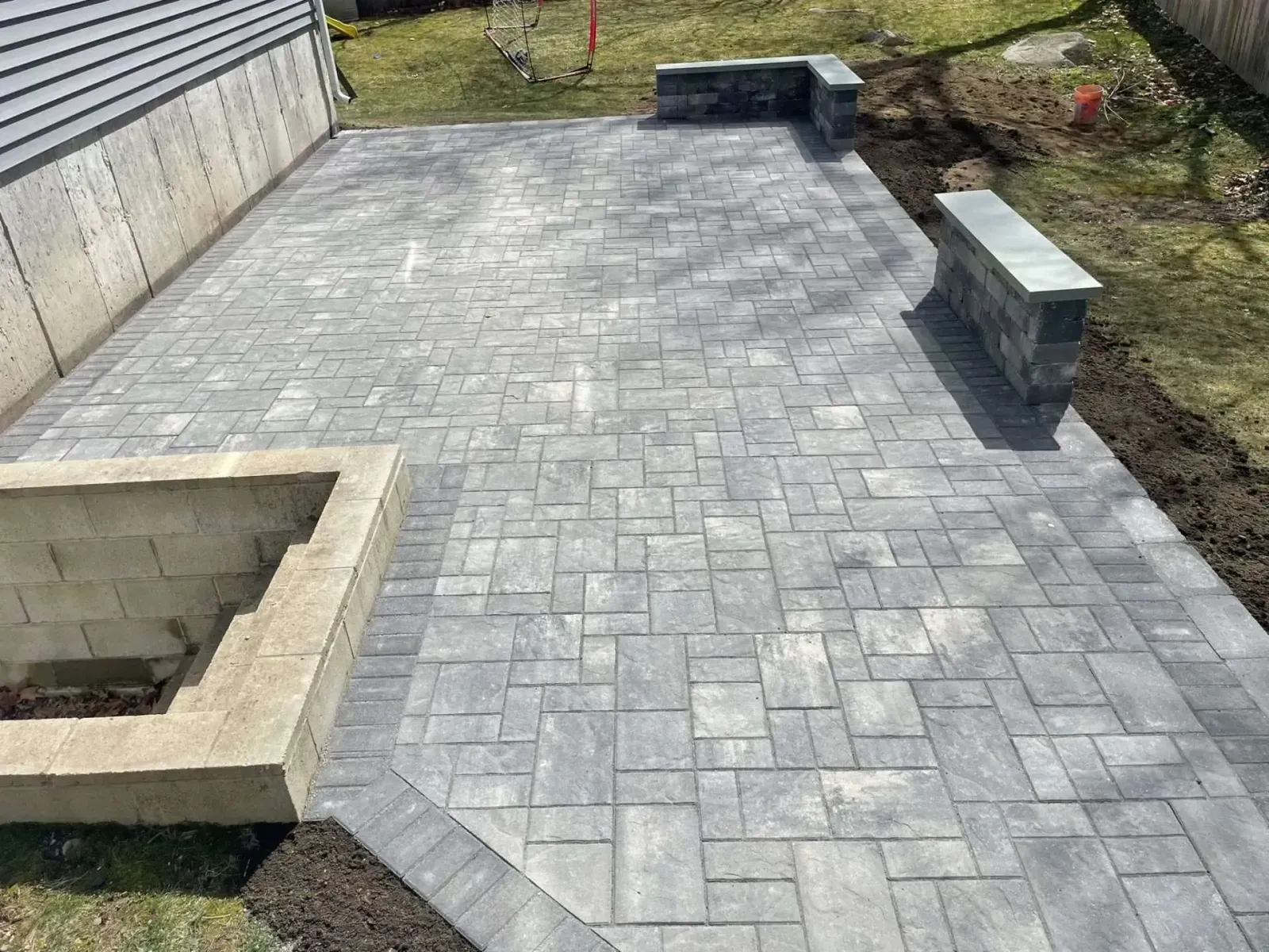 Stone patio with retaining walls next to a building and grass.