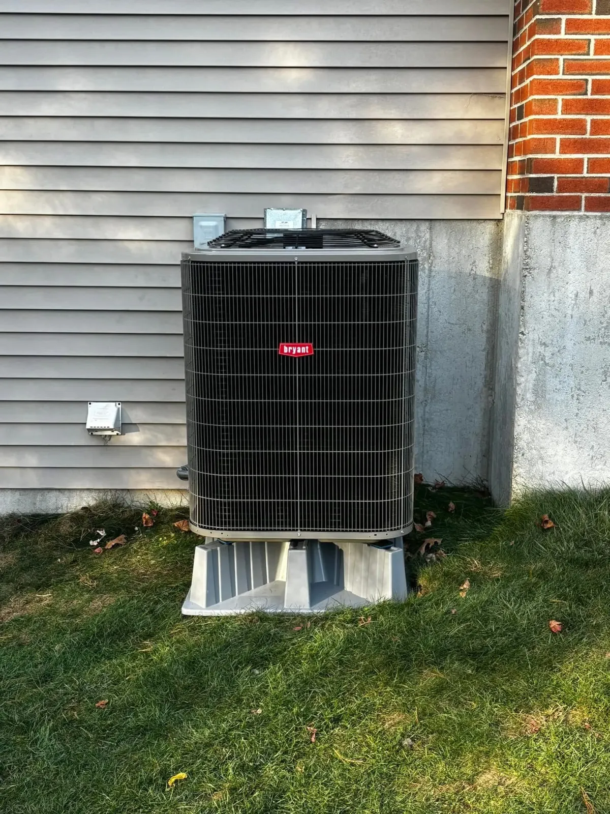 Bryant air conditioning condenser on a composite pad beside a brick chimney