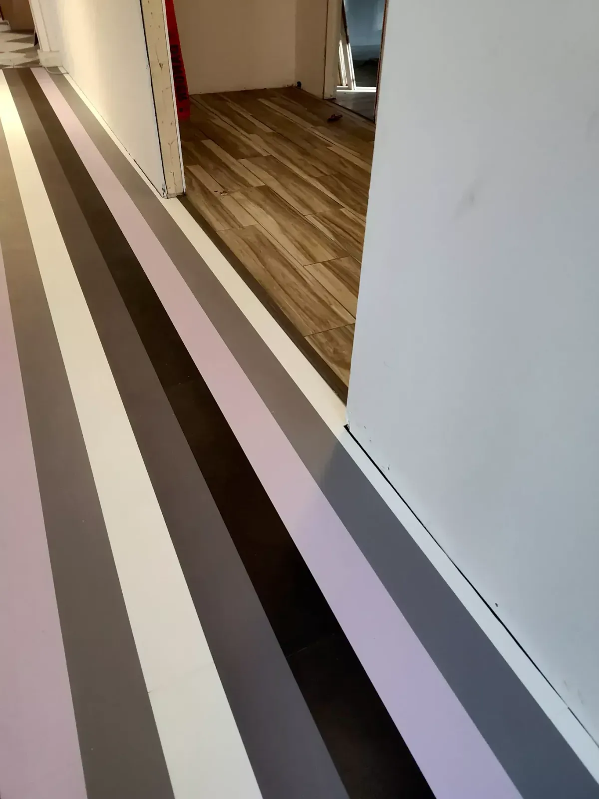A floor transition showing gray and purple striped flooring meeting a wood-look floor in a hallway.