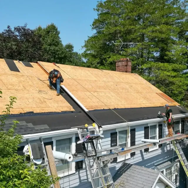 Roofing crew working on a residential roof installation, featuring plywood sheathing and black underlayment, with scaffolding and tools visible, showcasing commercial roofing services by Crown Roofing.