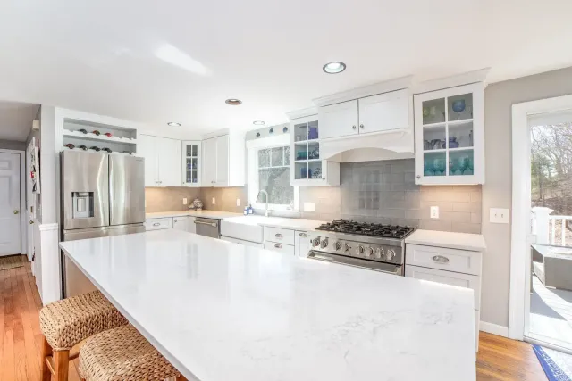 Bright white kitchen with marble island, stainless steel appliances, and large windows
