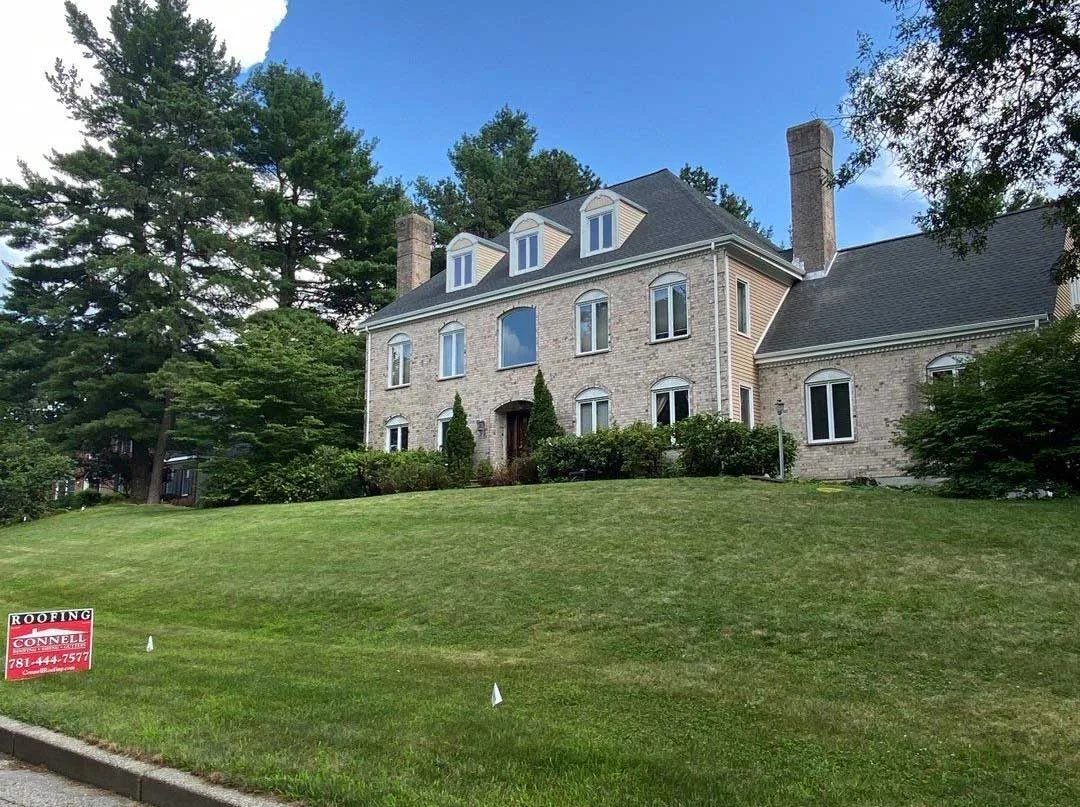 Large brick home with Connell Roofing sign displayed on front lawn