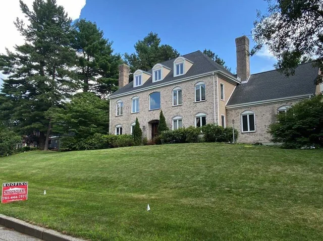 Large brick home with Connell Roofing sign displayed on front lawn