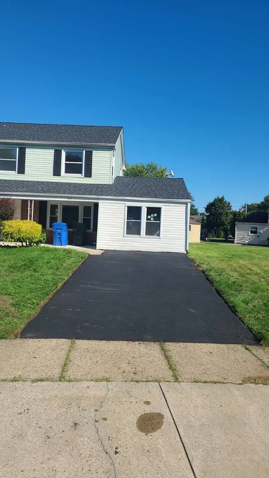 Two-story house with a black asphalt driveway. Blue sky.