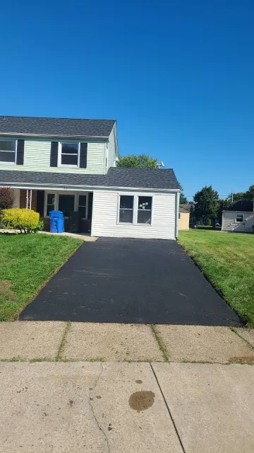 Two-story house with a black asphalt driveway. Blue sky.