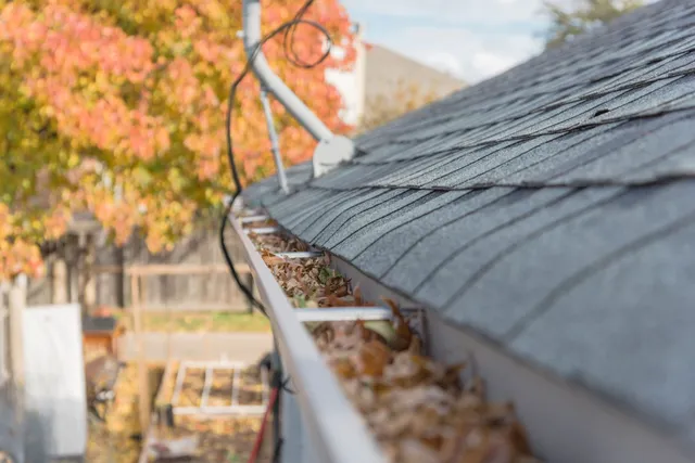 A gutter running along a shingle roof, filled with fallen autumn leaves