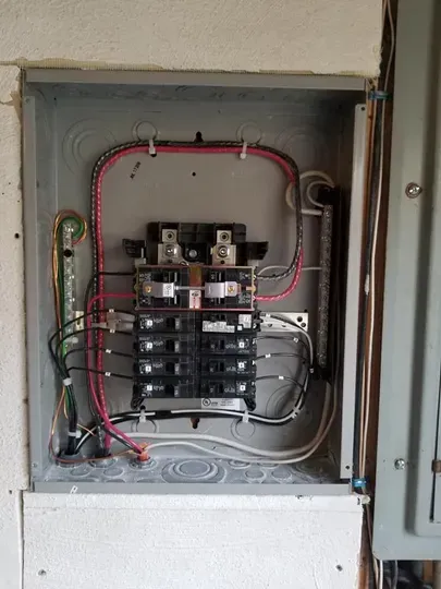 Open electrical breaker panel with red and white wiring inside a wall cabinet