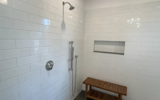 Minimalist shower with white subway tile walls, a rainfall showerhead, a handheld shower fixture, a recessed shelf, and a wooden bench.