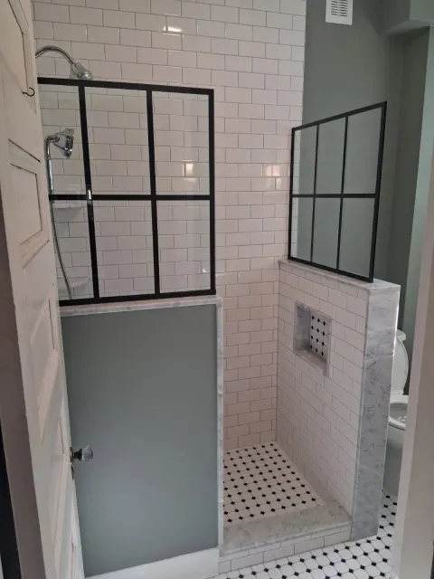 Small tiled shower area with black-framed glass panels and a frosted door.