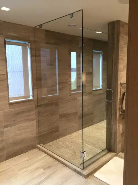 Glass shower enclosure in a tiled bathroom with three windows.