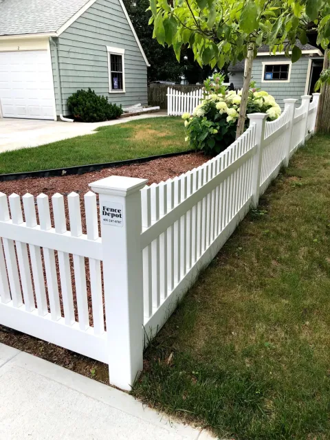 A white picket fence is in front of a house.