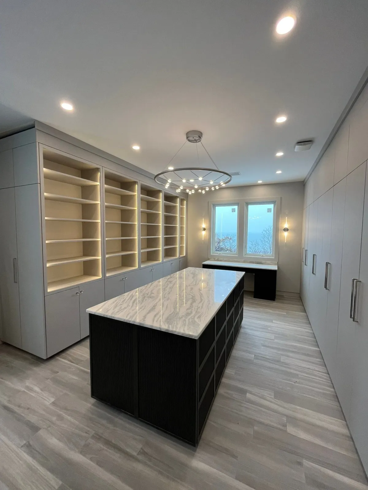 Modern kitchen with black and white cabinetry, a large marble island, built-in shelves, and a window view of trees and sky.