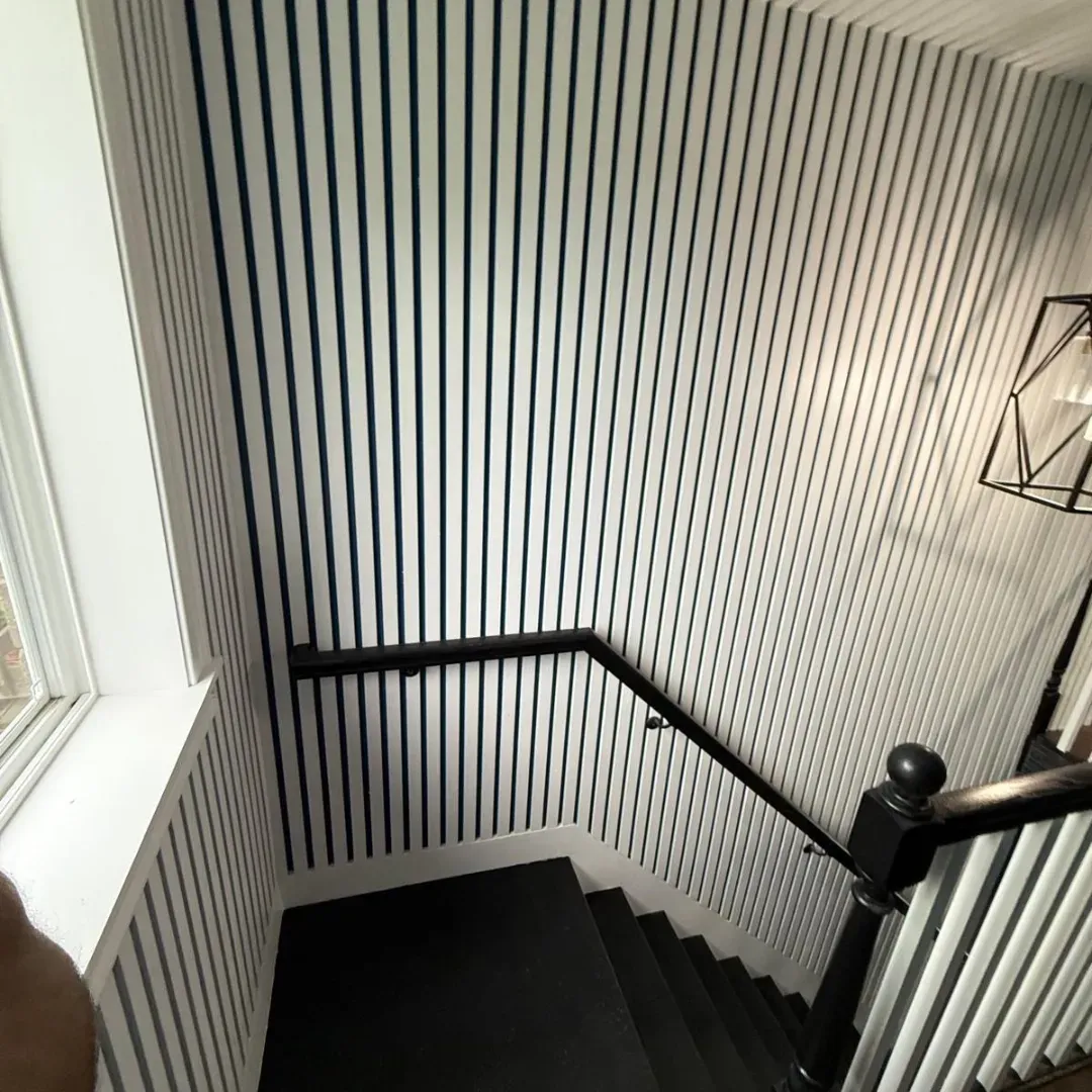 White and navy slat accent wall on stair landing in Winchester, MA — interior carpentry by Tinbercraft Construction