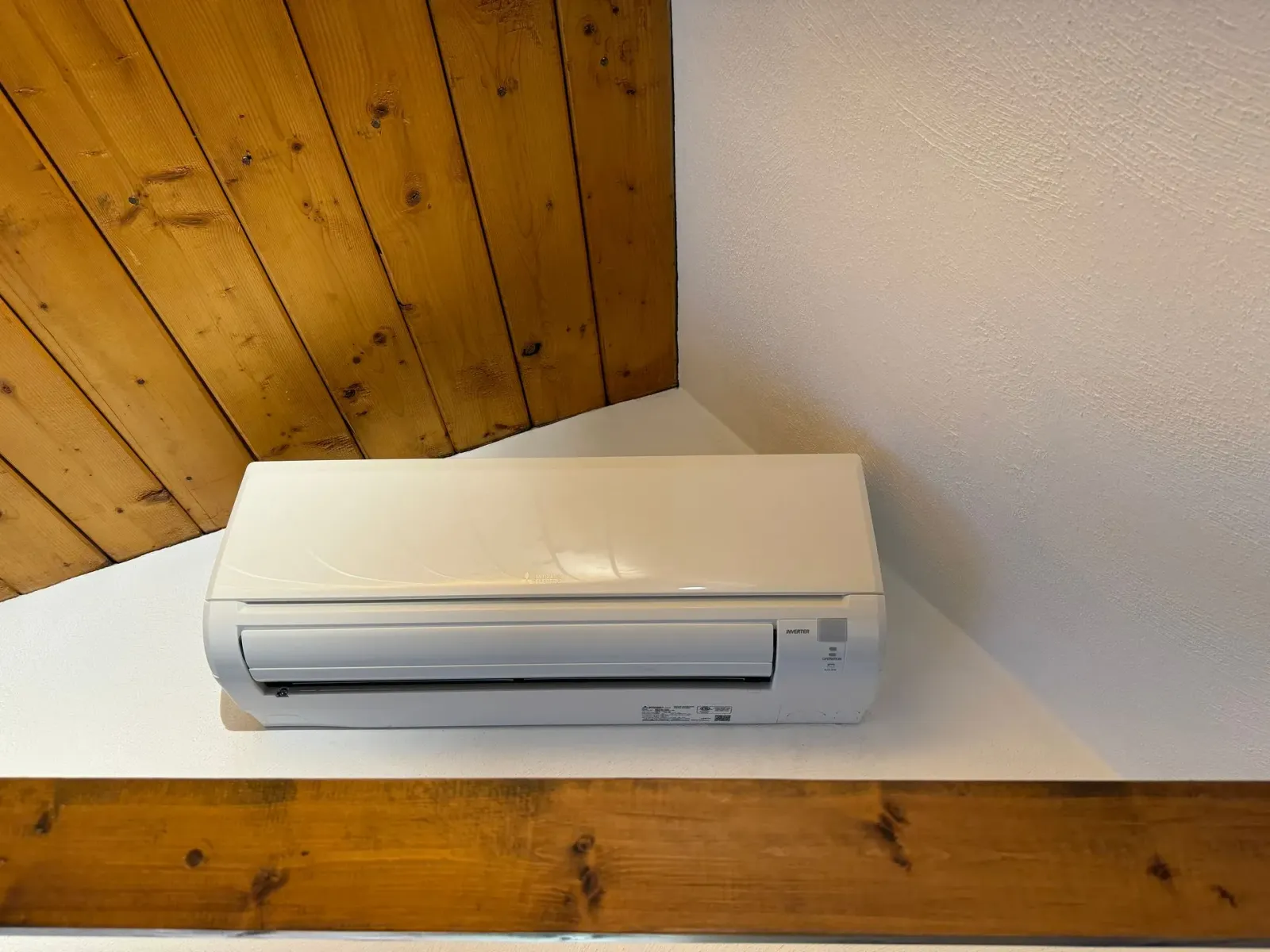 White air conditioner unit mounted in the corner of a room with wooden paneling and white walls.