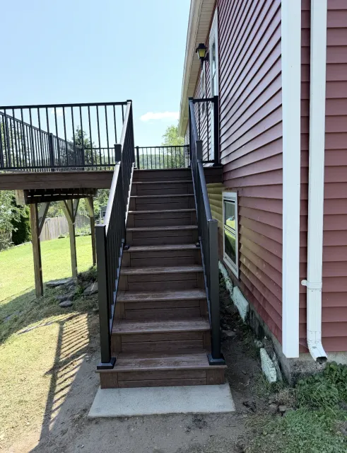Exterior wooden staircase beside a red house leading to a raised deck.