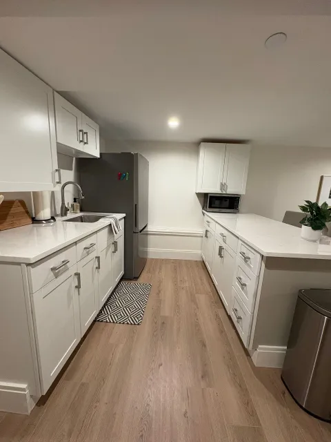 White kitchen with stainless steel refrigerator, white cabinets, and island with countertop.