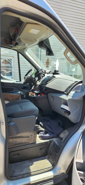 Open car door showing a cluttered front seat and dashboard inside a gray vehicle.
