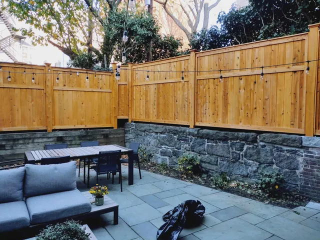 Cedar privacy fence above a stone retaining wall, bluestone patio