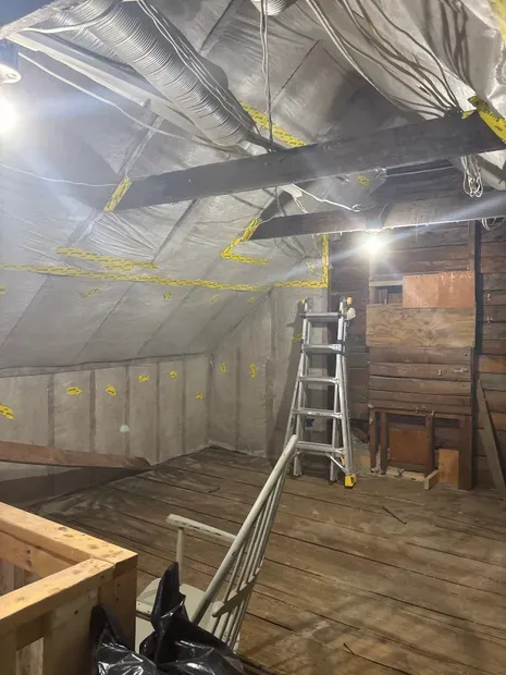 Attic under construction with foil insulation, ladder, exposed beams, and wooden floorboards