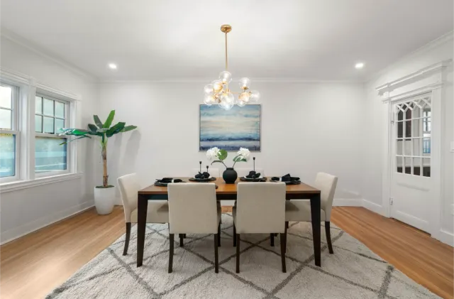 Modern dining room with six beige chairs, a wooden table, chandelier, and ocean-themed wall art.