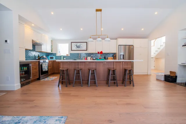 Open-plan kitchen with walnut island, blue tile backsplash and wide-plank floors