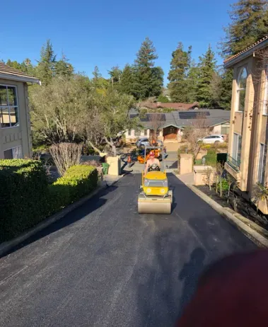 Yellow roller compacting fresh black asphalt on a residential driveway