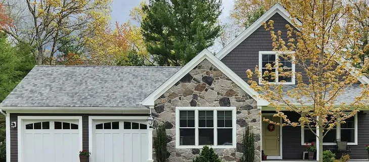 Suburban house with stone facade, white garage doors, and autumn trees in front