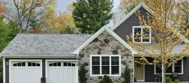 Suburban house with stone facade, white garage doors, and autumn trees in front