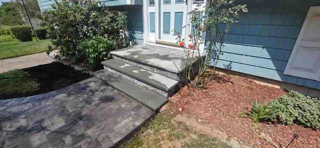 Front entry with concrete steps, blue siding, white doors, and landscaped mulch beds