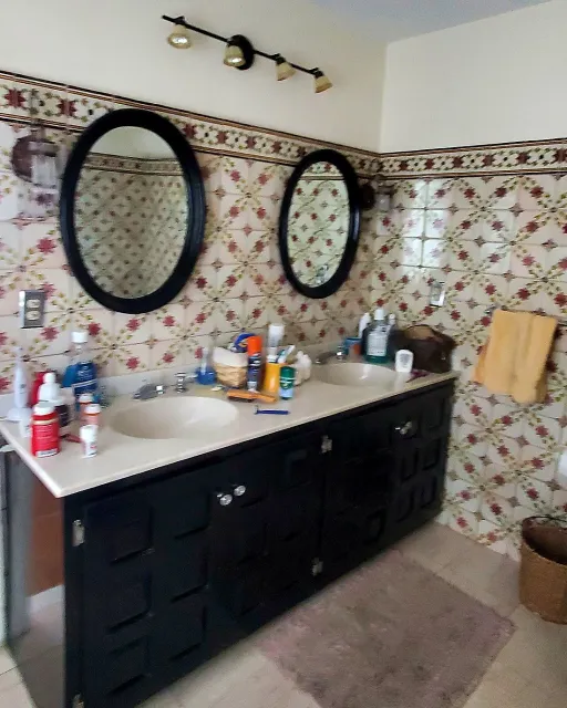 Dated master bathroom before remodeling, with patterned ceramic tile and a black double vanity
