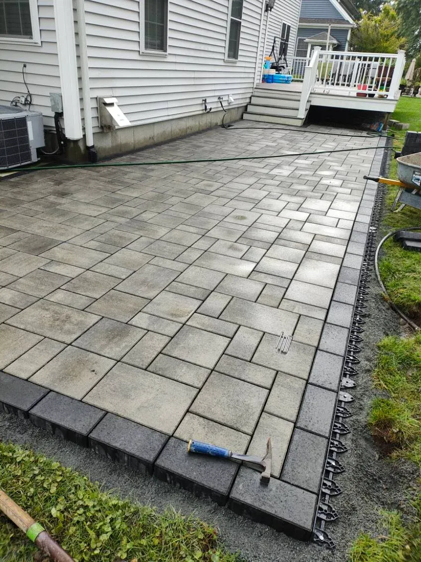 Newly installed stone paver patio with dark border beside residential deck