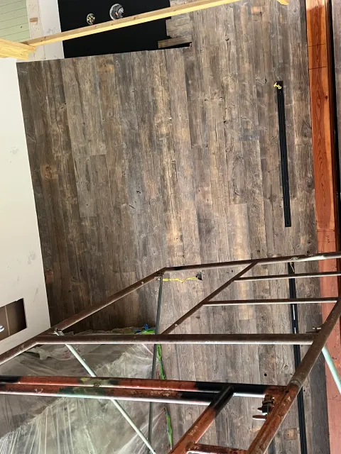 A room under renovation with a partially installed dark wood floor, scaffolding, and construction tools.