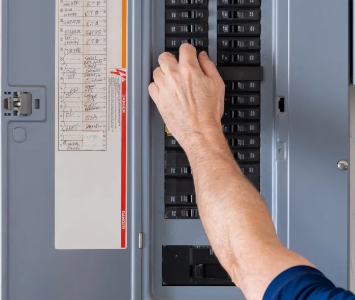 Hand reaching for circuit breaker switch in residential electrical panel with labeled circuits