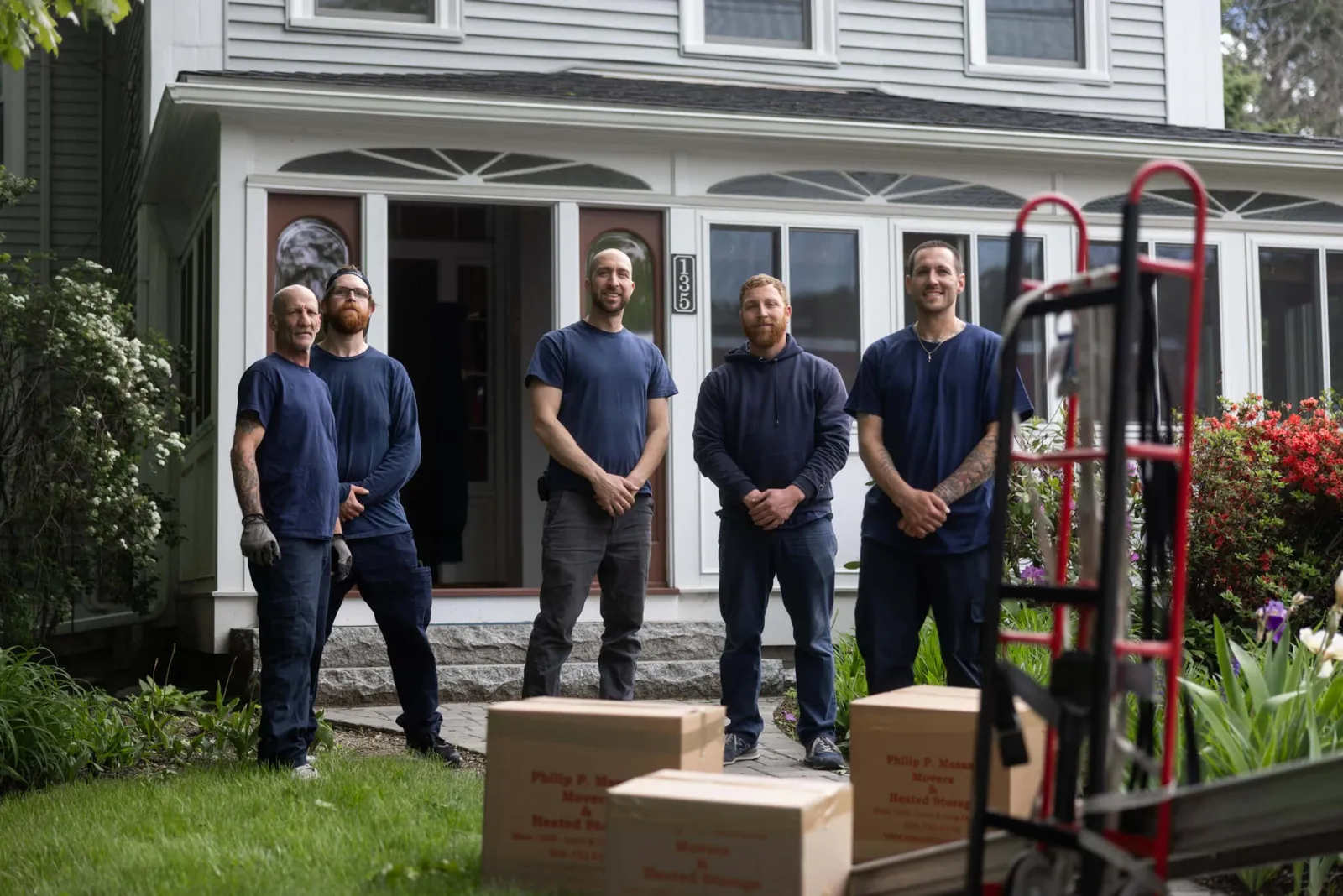 Five men standing in front of a house with boxes.