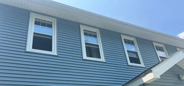 Blue-sided house with white-framed windows under a bright blue sky.