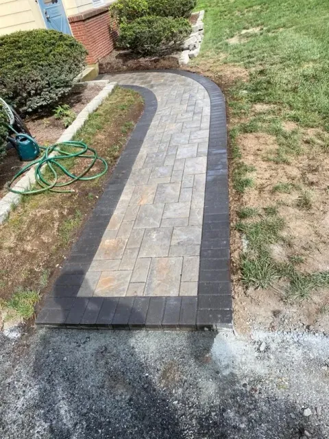 Curved brick garden walkway with dark border stones leading past lawn and shrubs