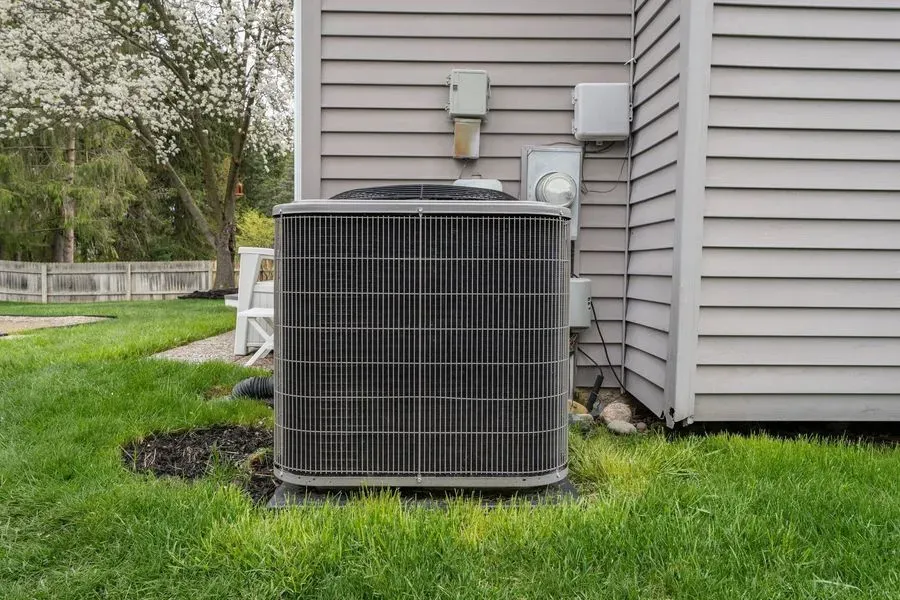Air conditioning unit outside a house with gray siding, sitting on green grass.