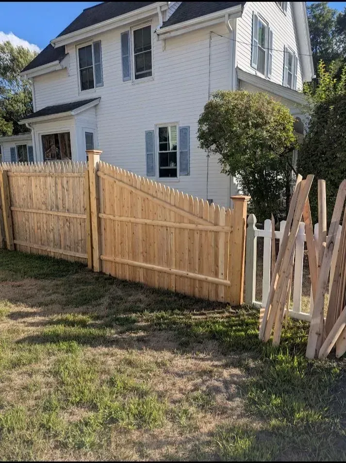 White two-story house with a slanted wooden fence and grassy yard