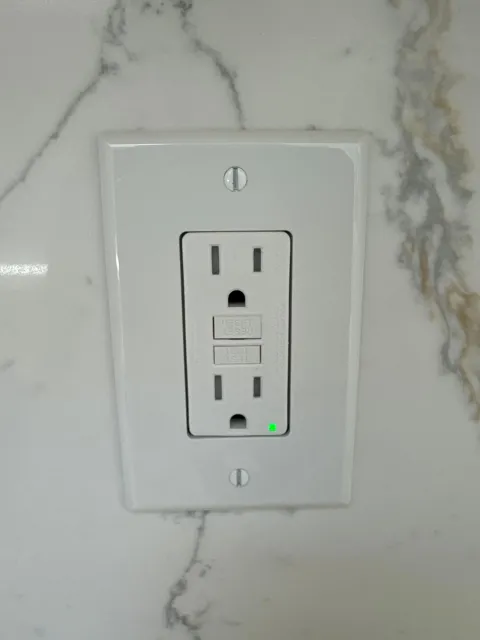 Electrical outlets and switch with exposed wiring set in a gray wall.