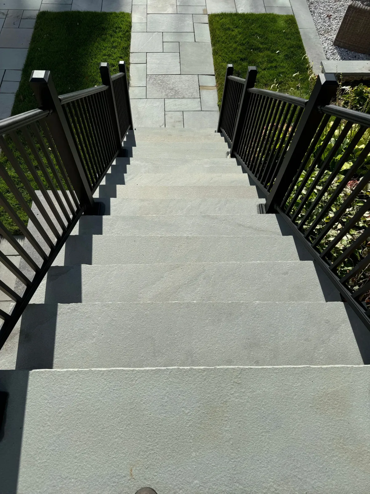 A set of stairs with a black railing leading up to a grassy area.