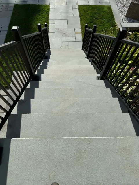 A set of stairs with a black railing leading up to a grassy area.