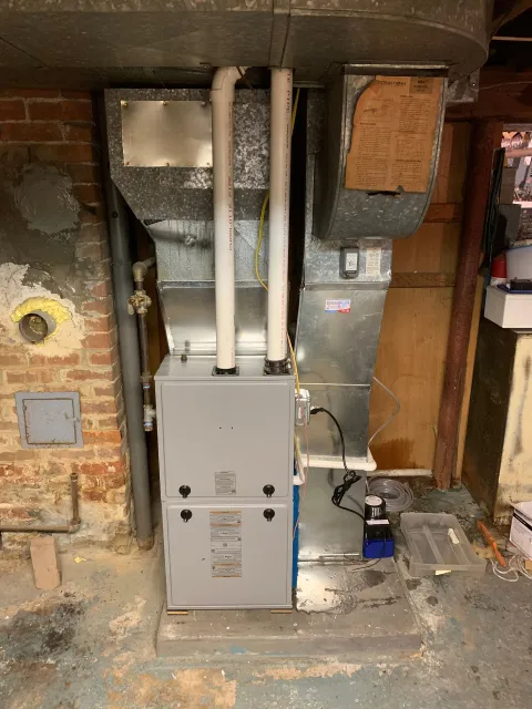 An air conditioner is sitting in a basement next to a brick wall.