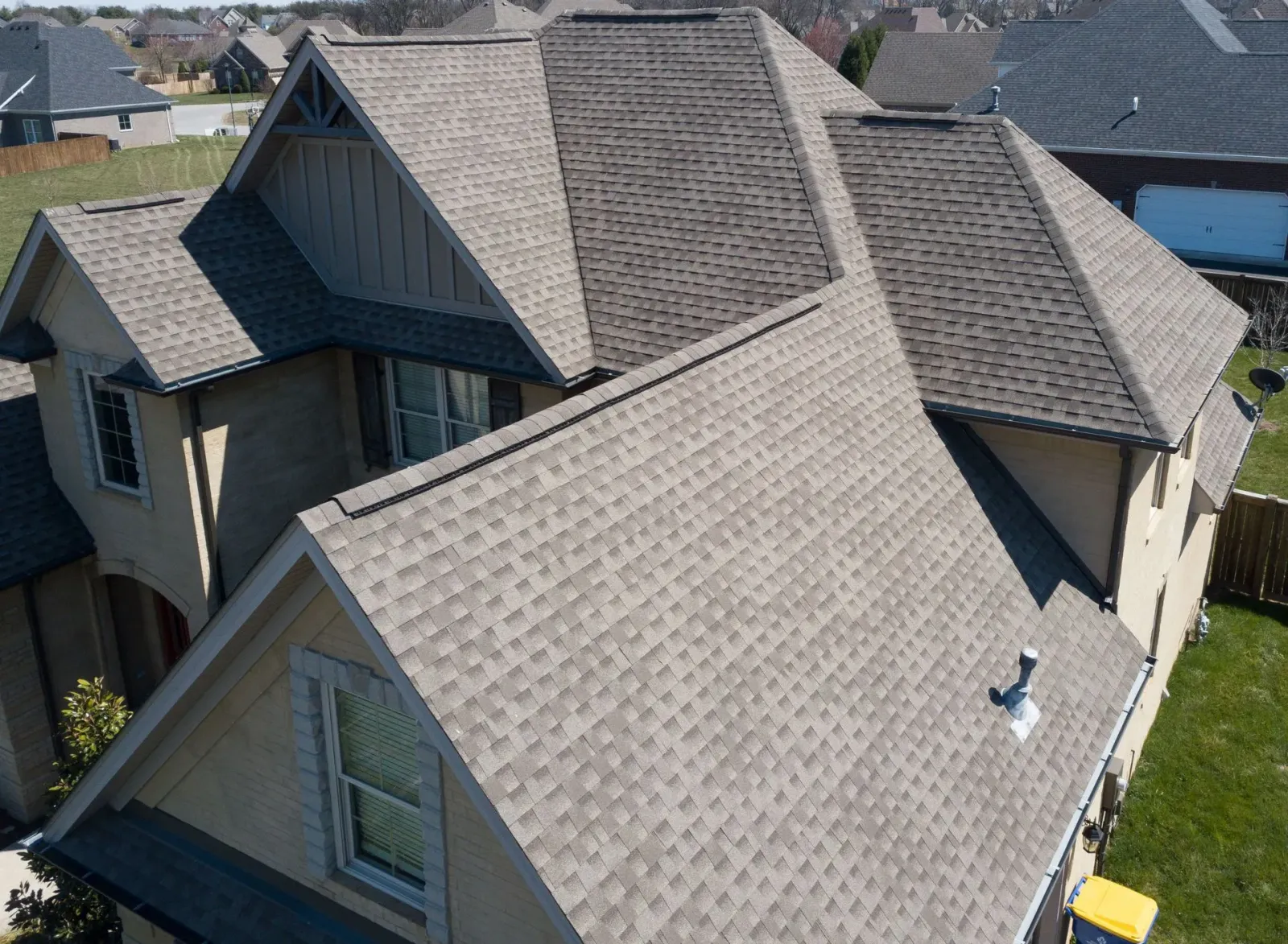Tan house with complex, gray shingle roof. Exterior view from above.