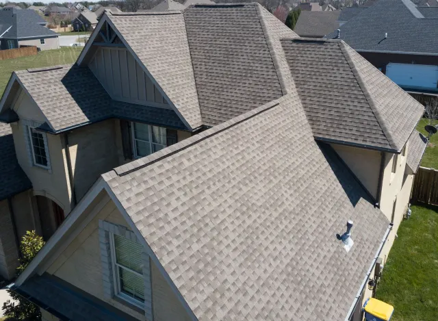 Tan house with complex, gray shingle roof. Exterior view from above.