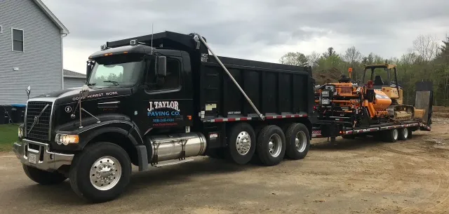 A dump truck with a trailer attached to it is parked in front of a house.