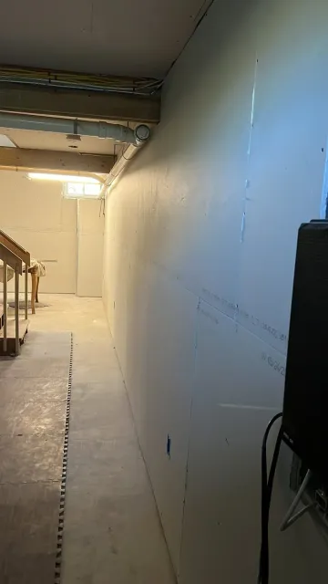 Basement drywall installation in progress with fresh sheets hung along concrete block walls